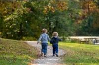 Due bambini di spalle che corrono felici in un prato verde a Stigliano, in Basilicata