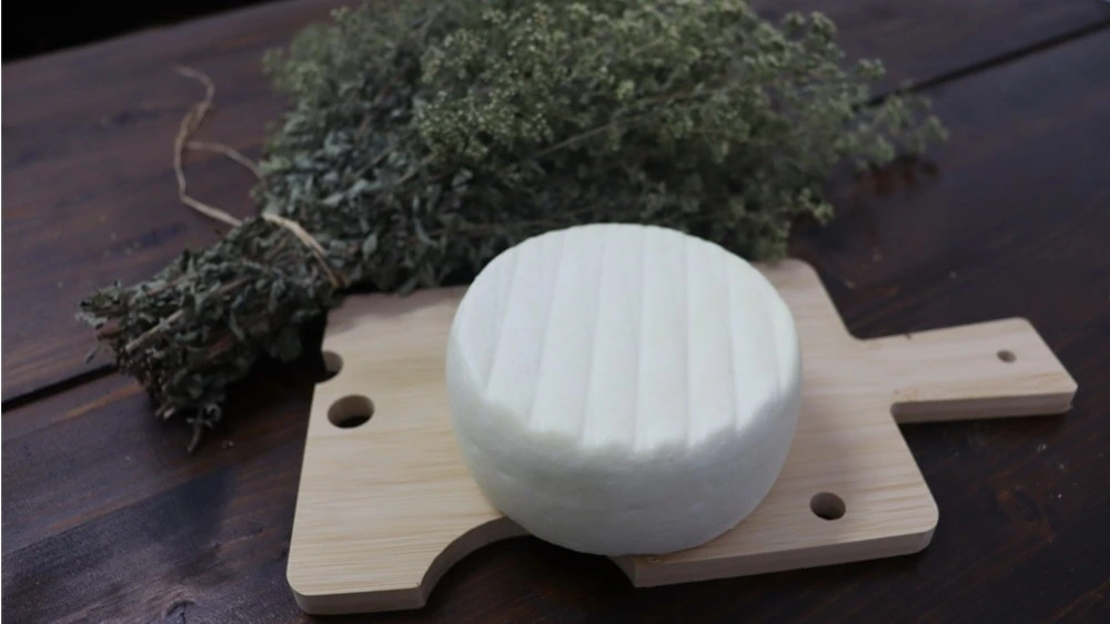 Forma di formaggio fresco artigianale della Latteria Donna Tina su tagliere di acero con rosmarino
